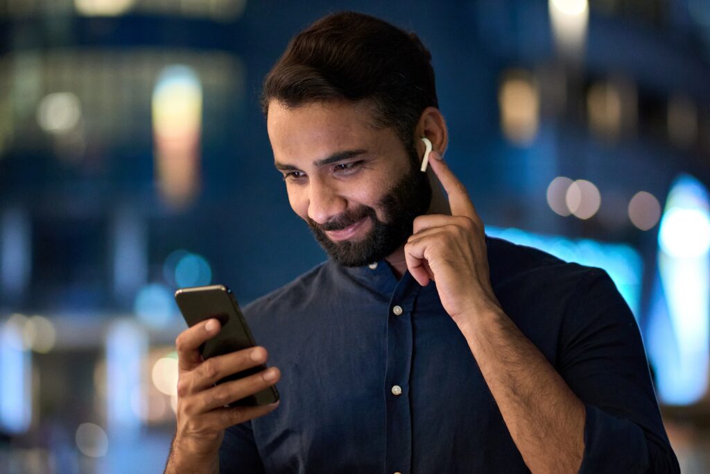 A man holding a smartphone and wearing earbuds. 